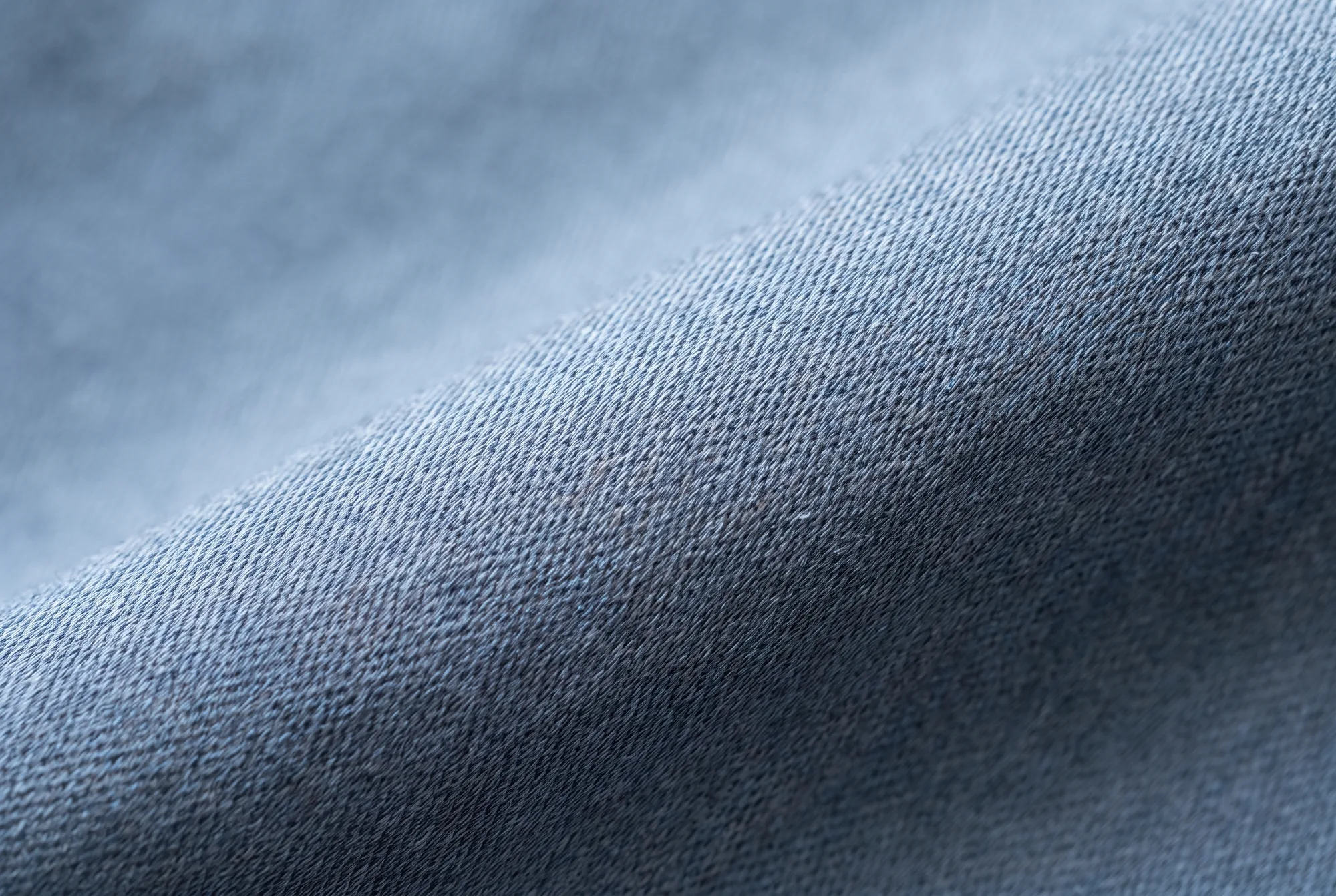 A macro view of slate bamboo-fibre cloth, the fine flat weave and a single soft fold catching cool light.